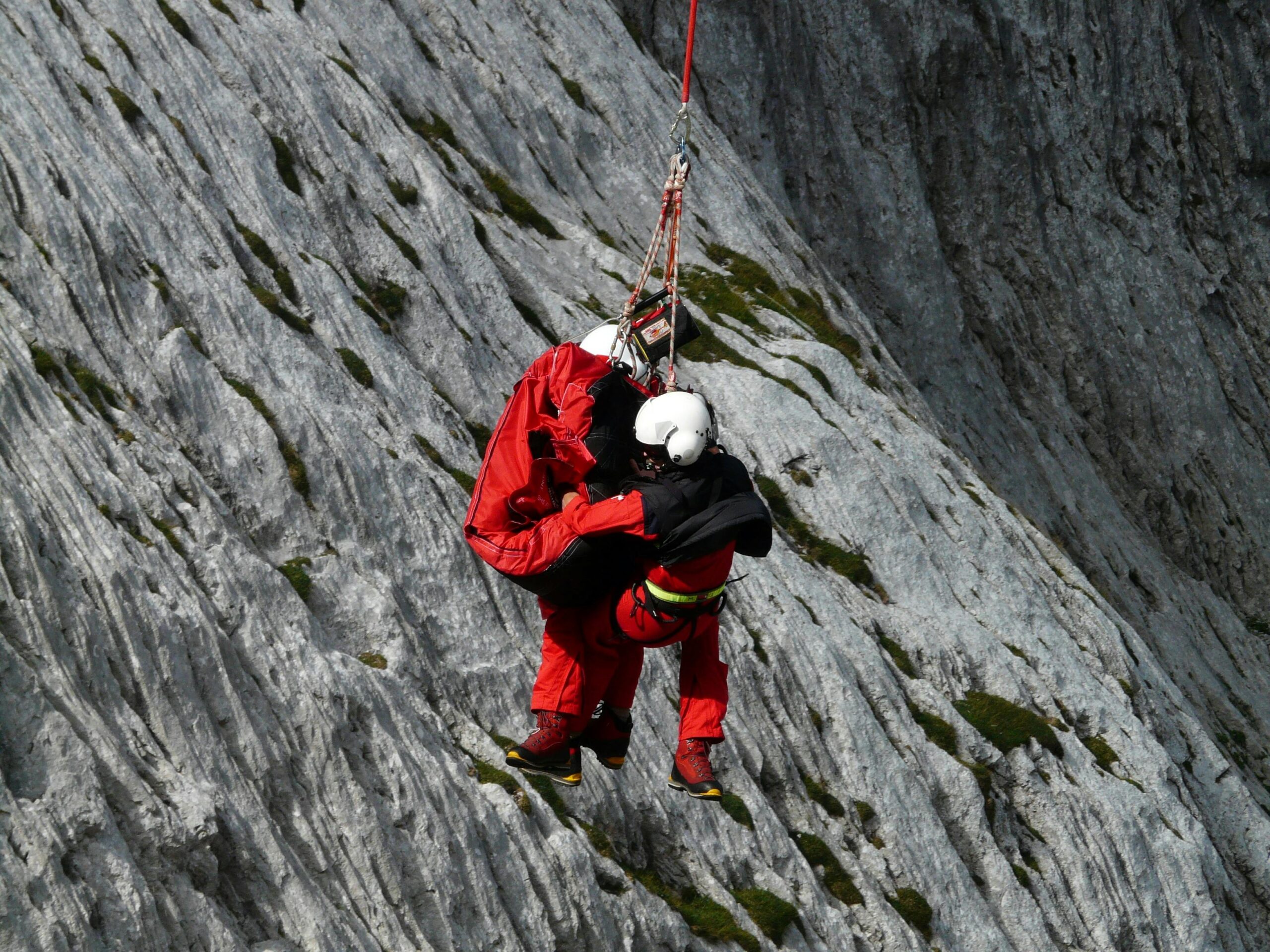 Two rescuers in action on a mountain, showcasing teamwork and safety in a daring lift.