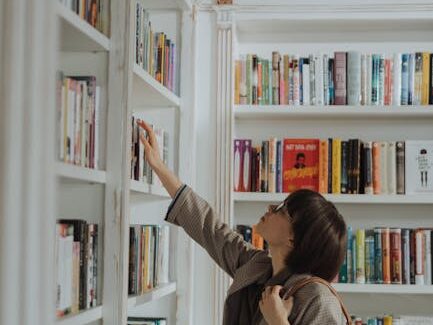 A young woman reaching for a book on a stylish library bookshelf, embodying education and leisure.