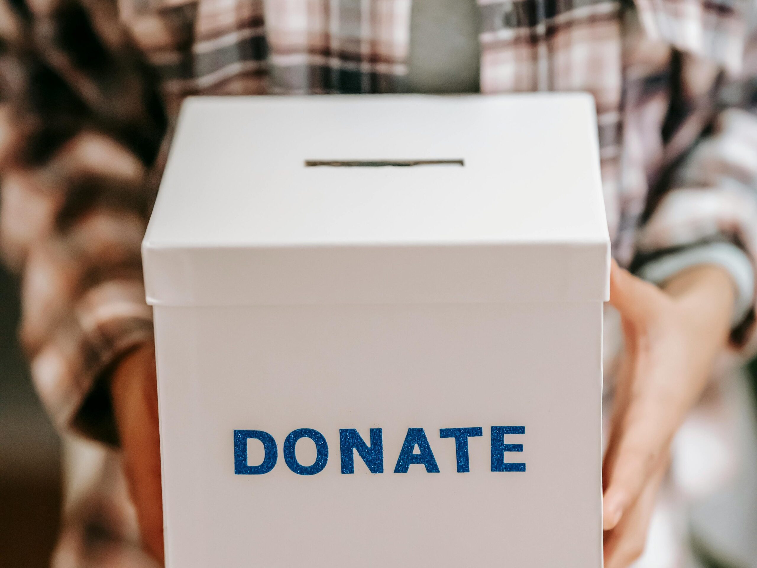 Close-up of a person holding a 'donate' box, encouraging charity and support.